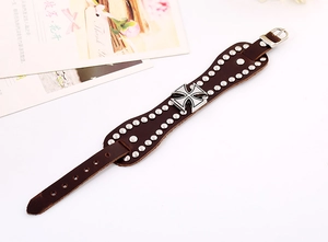 Detail of a wide brown leather punk bracelet featuring metal studs and an iron cross charm