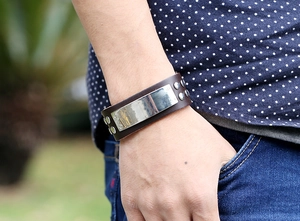 Close-up of wide brown leather cuff bracelet with polished silver plate and metal rivets