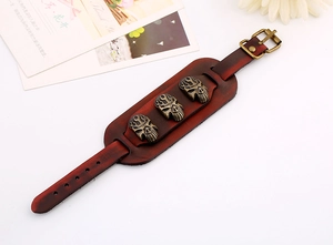 Détail d'un bracelet punk large en cuir marron avec trois crânes en bronze et boucle