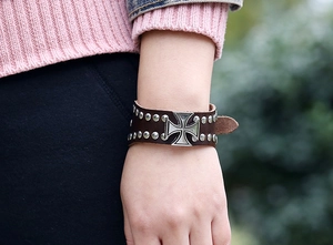 Detail of a brown punk leather bracelet with silver studs and an iron cross ornament