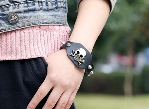 Close-up of punk black leather bracelet with silver skull emblem and metal cone spikes