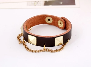 Macro detail of dark brown leather punk bracelet with gold studs and chain links