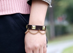 Detail of a brown leather punk bracelet with gold square studs and chain accent