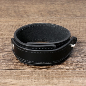 Minimalist black wide leather bracelet with silver metal studs on a wooden background