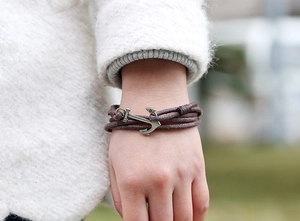 Detail of multi-layer wax cord bracelet featuring a vintage silver anchor clasp on wrist