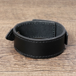 Detail of minimalist black wide leather bracelet with stitching on wooden surface
