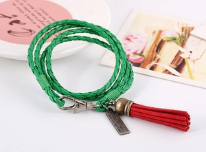 Detalle de pulsera de cuero trenzado verde con borla roja y colgante de metal grabado