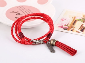 Detalle de pulsera de cuero trenzado rojo de varias capas con placa de metal y borla larga