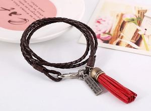 Detalle de pulsera de cuero trenzado con borla roja y placa de metal plateado grabada