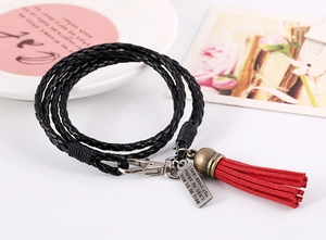 Detalle de pulsera de cuero multicapa con borla roja y placa de metal con grabado