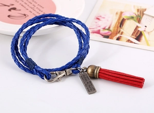 Detalle de pulsera bohemia tejida azul multicapa con dije de bronce y borla roja suave