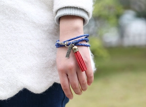 Detalle de pulsera de cuero trenzado multicapa con borla roja y etiqueta de bronce