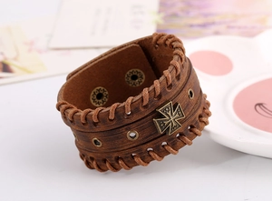 Detail view of brown leather cuff with braided edges and a vintage cross metal badge
