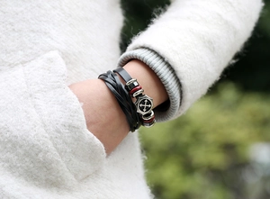 Detail of multi-layer leather bracelet with metallic arrow pendant and red accents on wrist