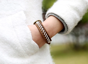 Détail d'un bracelet en cuir marron foncé avec couture blanche sur un pull doux