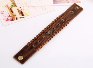 Close-up of vintage leather bracelet featuring a cross charm and woven edges