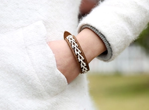 Nahaufnahme eines braunen Lederarmbands mit weißem Geflecht am Handgelenk
