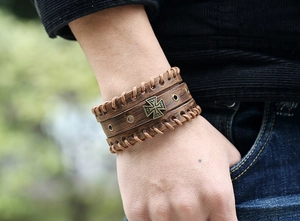 Macro view of brown vintage leather bracelet featuring a bronze cross emblem and woven edges