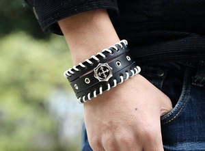 Détail d'un bracelet punk en cuir noir avec badge flèche croisée et bords tressés