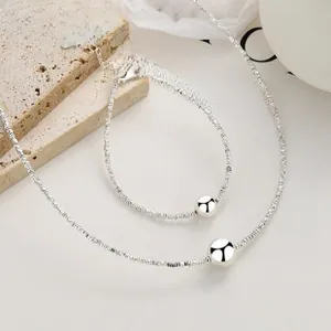 Polished silver beaded necklace and bracelet set on a decorative stone base