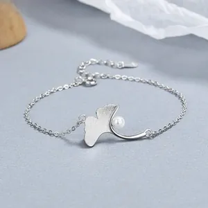 Macro detail of silver ginkgo leaf charm with a white pearl on a 925 silver chain