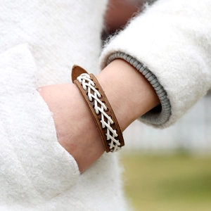Vintage braunes Lederarmband mit weißer Kreuznaht-Webung auf weichem Hintergrund