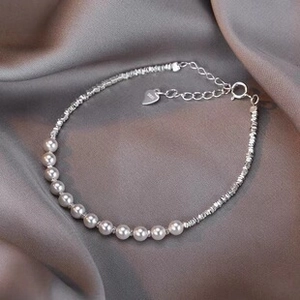 Detailed shot of S925 silver pearl bracelet with heart charm on dark grey silk fabric