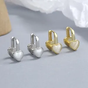 Close-up of gold and silver heart earrings with opal stones on a textured backdrop