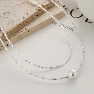 Macro detail of 925 sterling silver layered chain with elegant round white pearl charm