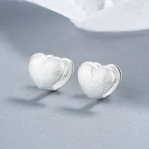 Macro shot of 925 sterling silver heart earrings with a brushed matte finish on a blue base