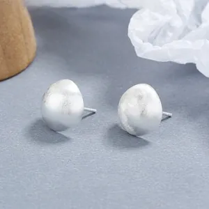 Detail of matte brushed S925 sterling silver half-ball stud earrings on a textured surface