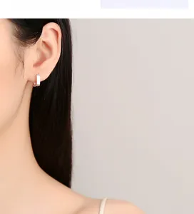 Close-up of a minimalist silver square hoop earring on a model's ear with a mirror finish