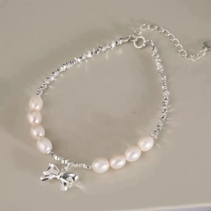 Detail of silver bow pendant and freshwater pearls on a crushed silver chain bracelet