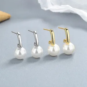 Macro shot of 925 silver and gold pearl stud earrings with minimalist curved hook design