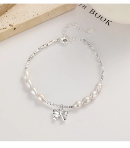 Detail of S925 silver bow pendant and baroque pearls on an elegant chain bracelet