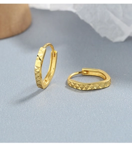 Close-up of gold faceted hoop earrings with geometric diamond-cut texture and shiny finish