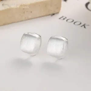 Macro shot of silver brushed square stud earrings showing matte metal texture and finish