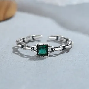 Macro detail of silver chain ring featuring emerald green square zircon and open band