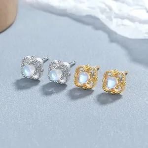 Detail view of gold and silver cat moonstone stud earrings on a blue textured background