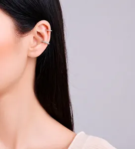Dettaglio di due ear cuff d'argento a forma di C con zirconi indossati sull'orecchio del modello