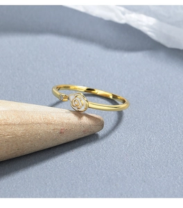 Detail of 18K gold ring with white enamel rose and sparkling crystal on wood