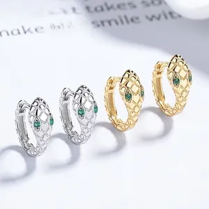 Macro detail of snake-head hoop earrings featuring green stone eyes and scale textures