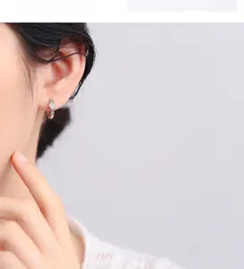 Close-up of diamond-encrusted silver rhombus hoop earrings worn on female ear model