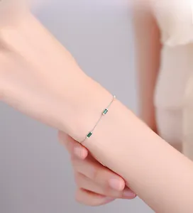 Close-up of minimalist silver box chain bracelet with rectangular green emerald gemstones
