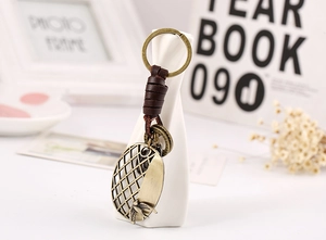 Detail of vintage brown leather keychain with bronze swallow pendant on a white vase