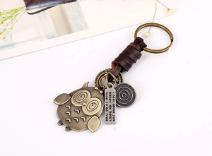 Detailed close-up of retro leather keychain with bronze owl pendant and engraved metal tags