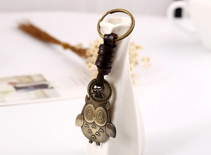 Detailed shot of bronze owl charm with braided leather strap on a white vase