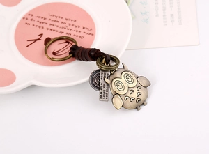 Close-up of bronze owl keychain with braided leather cord on a decorative ceramic plate