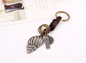 Détail d'un porte-clés vintage en cuir avec pendentif conque et plaque en métal gravée
