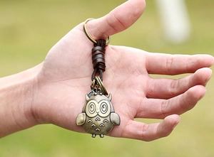 Close-up of vintage bronze owl pendant with woven leather strap held in hand